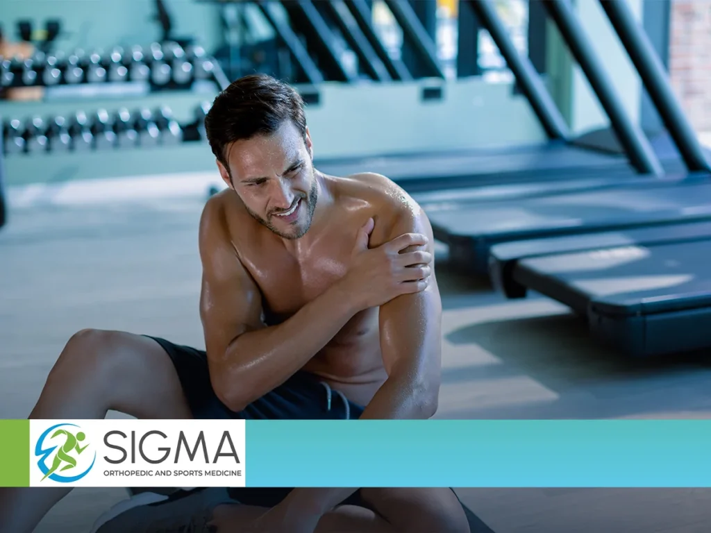 A shirtless man clutching his painful shoulder